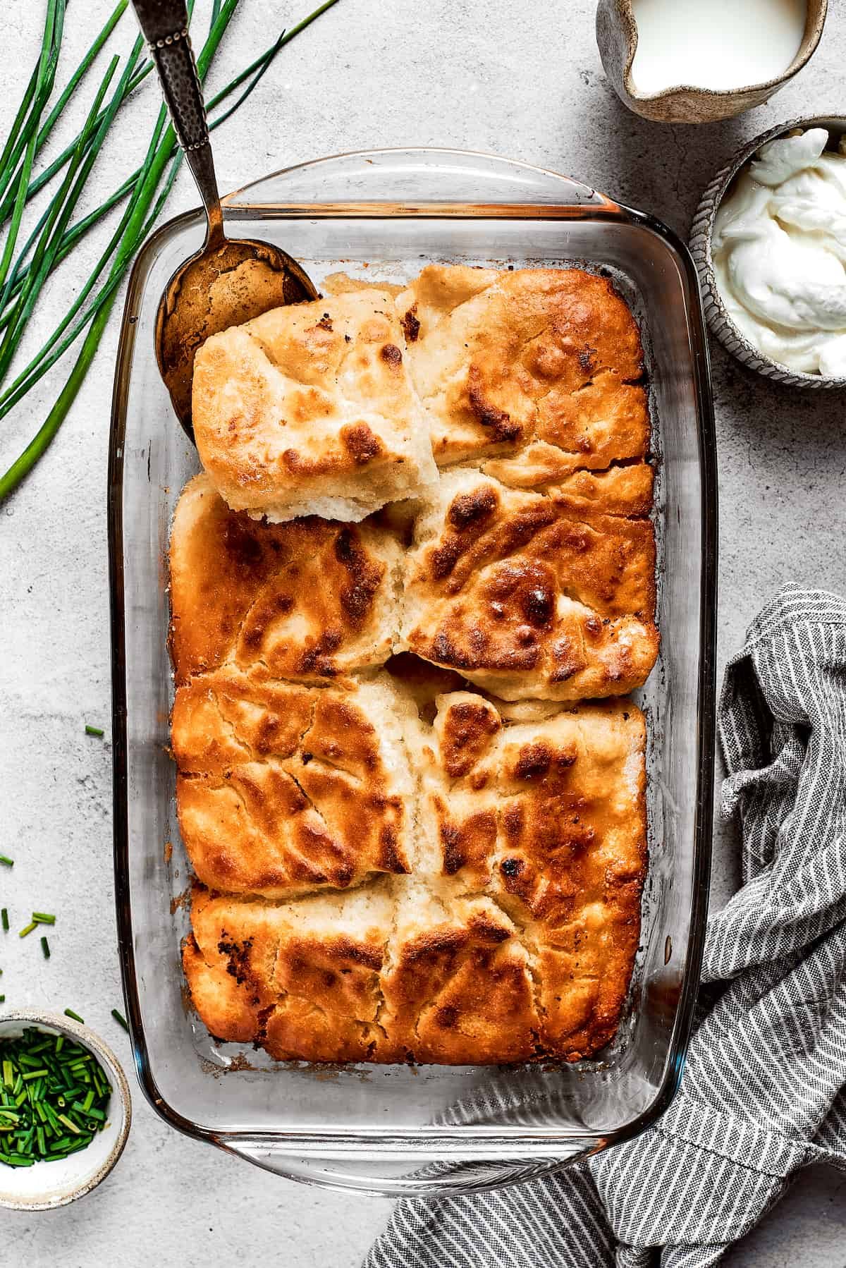 Overhead view of a baking dish full of butter swim biscuits, with a serving spoon removing a corner piece