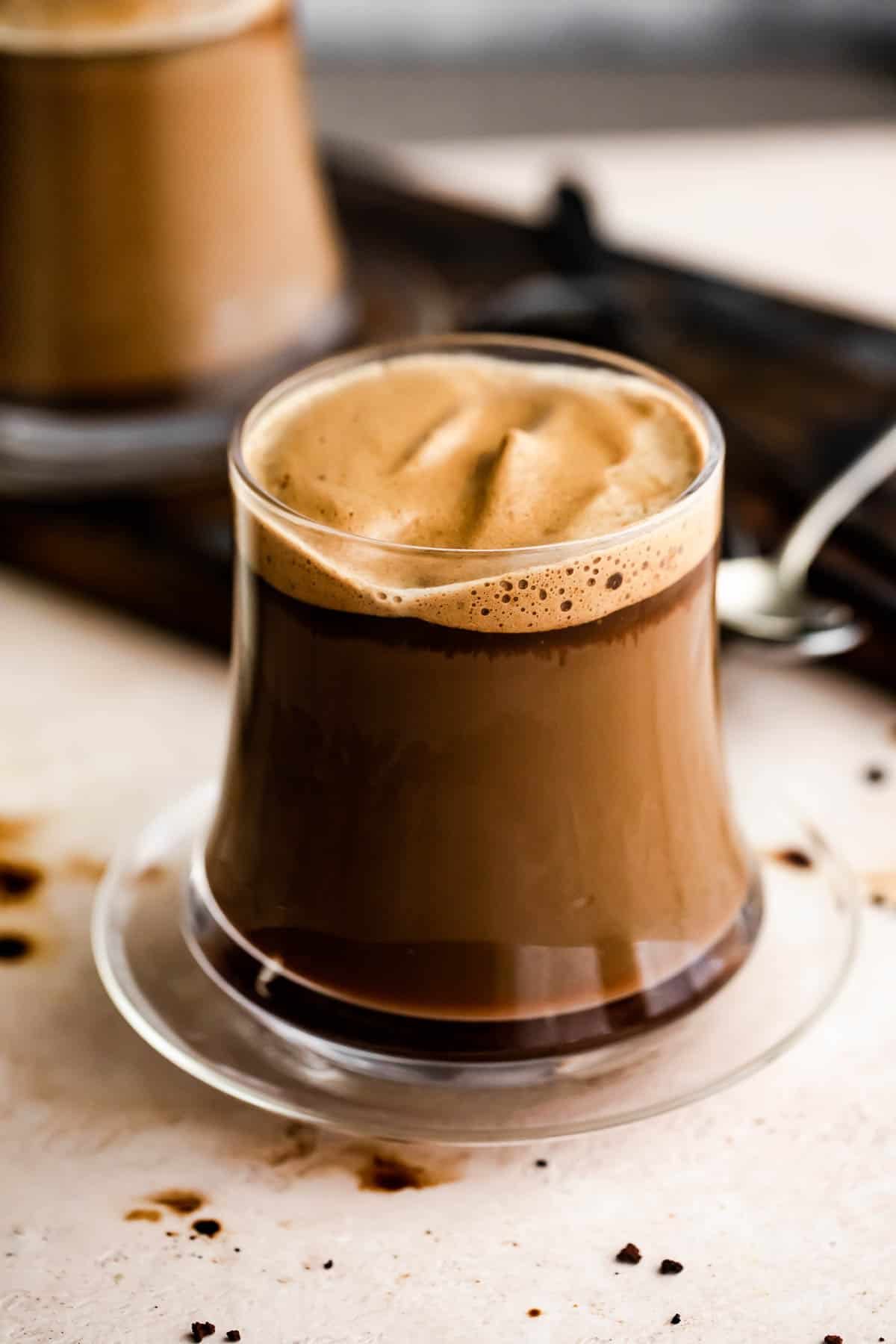 A glass mug with Caffe Macchiato and another mug set right behind it.