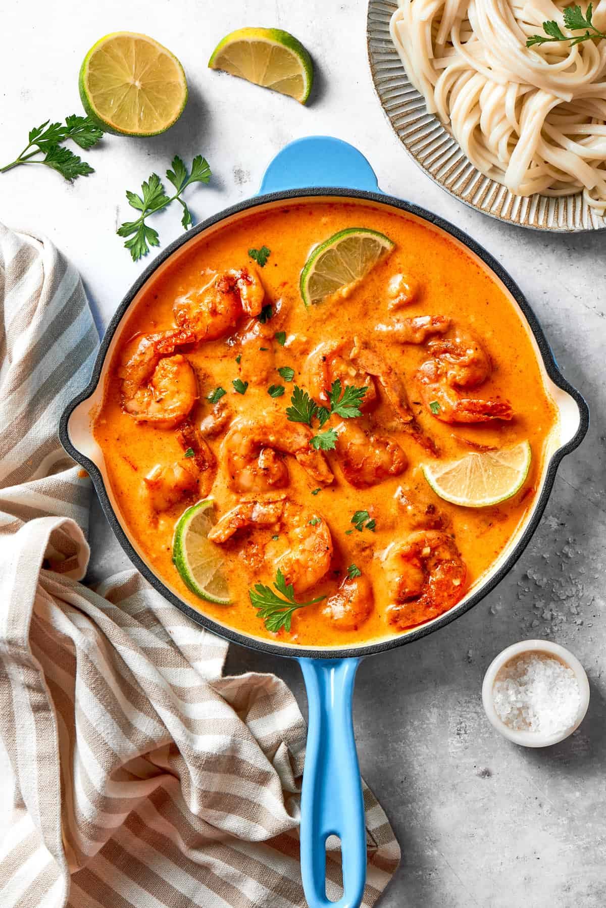 A skillet of cajun shrimp in tomato sauce, with lime wedges placed around the shrimp and a garnish of fresh herbs.