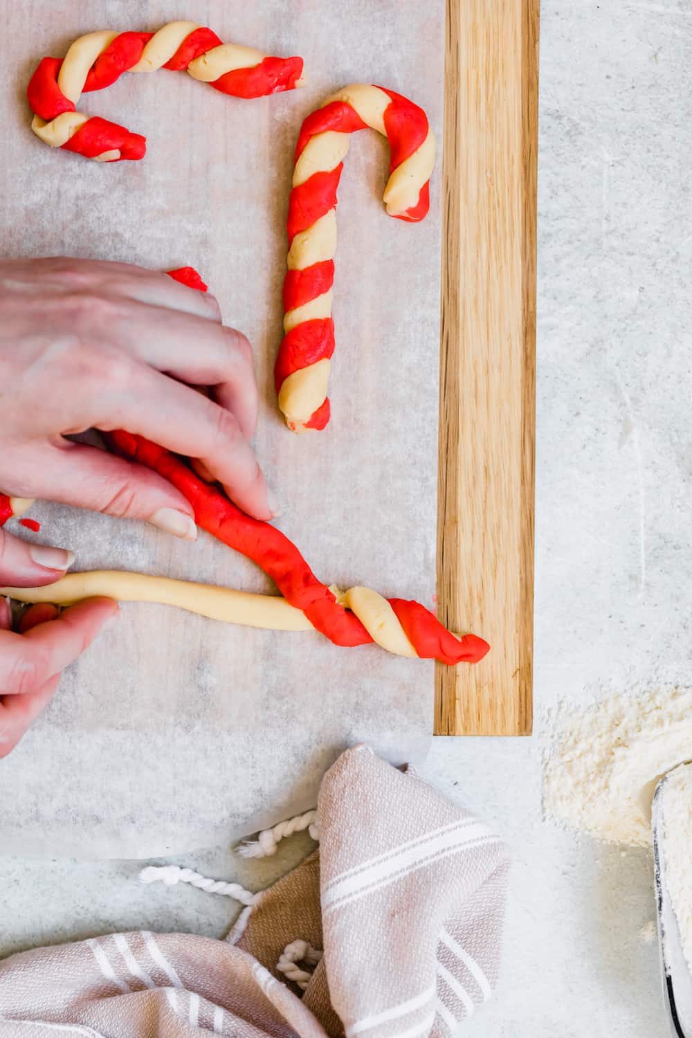 Two Shaped Candy Cane Cookies Next to A Third Being Shaped by Two Hands