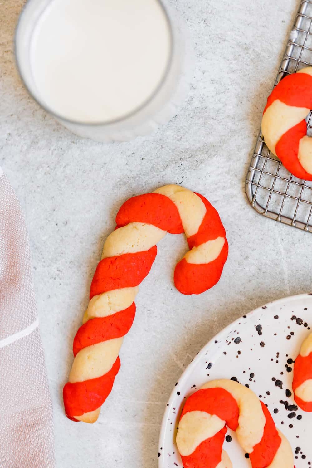 A Single Cookie on the Counter Next to a Plate Holding More Candy Cane Cookies