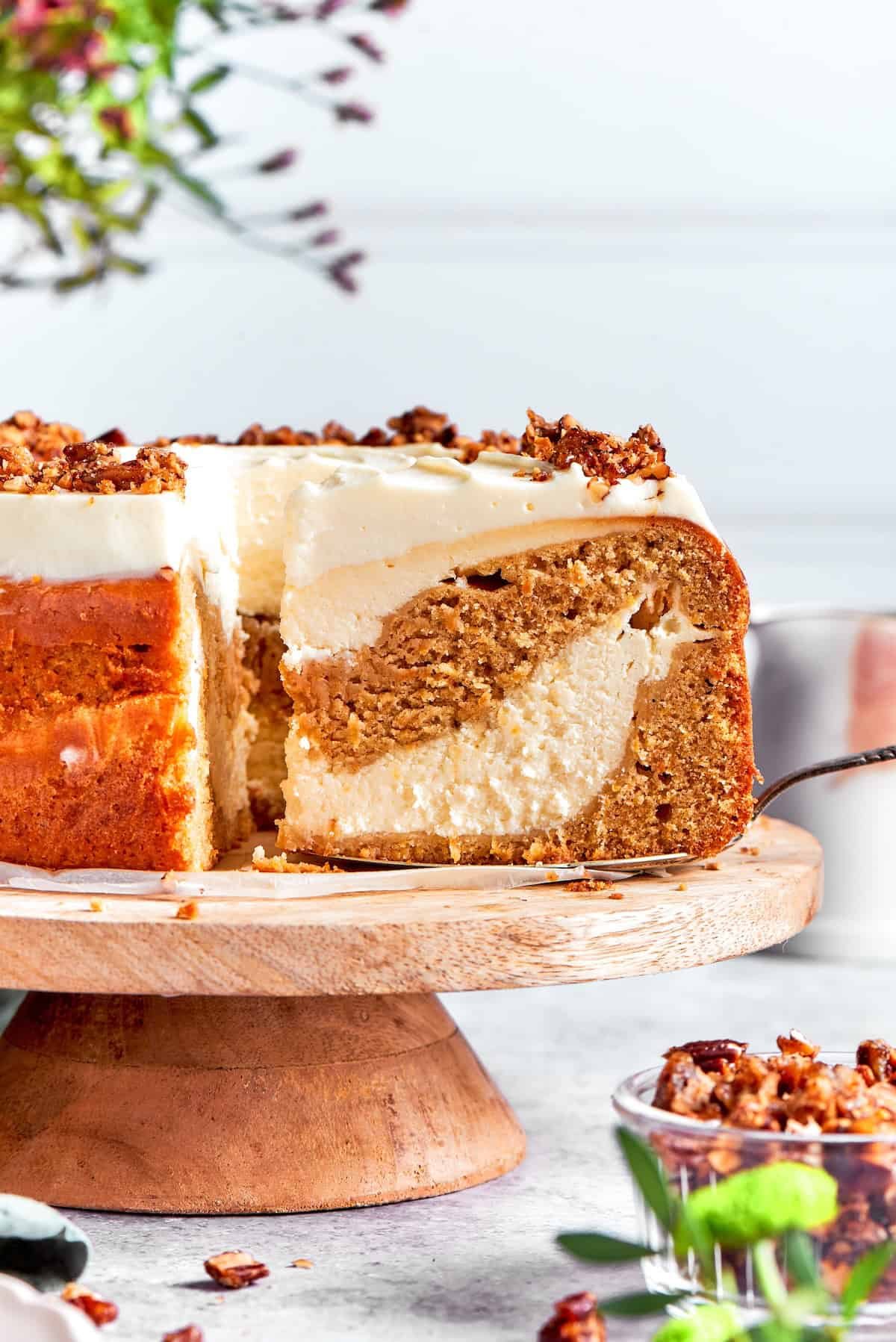 A slice is removed from a platter of carrot cake cheesecake.