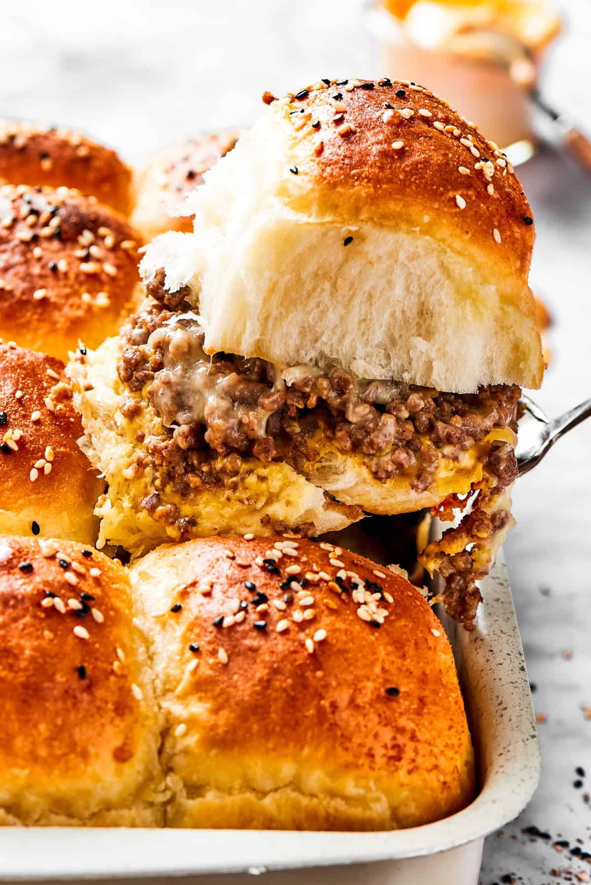 A spatula holding up a sandwich with burger buns filled with ground meat.