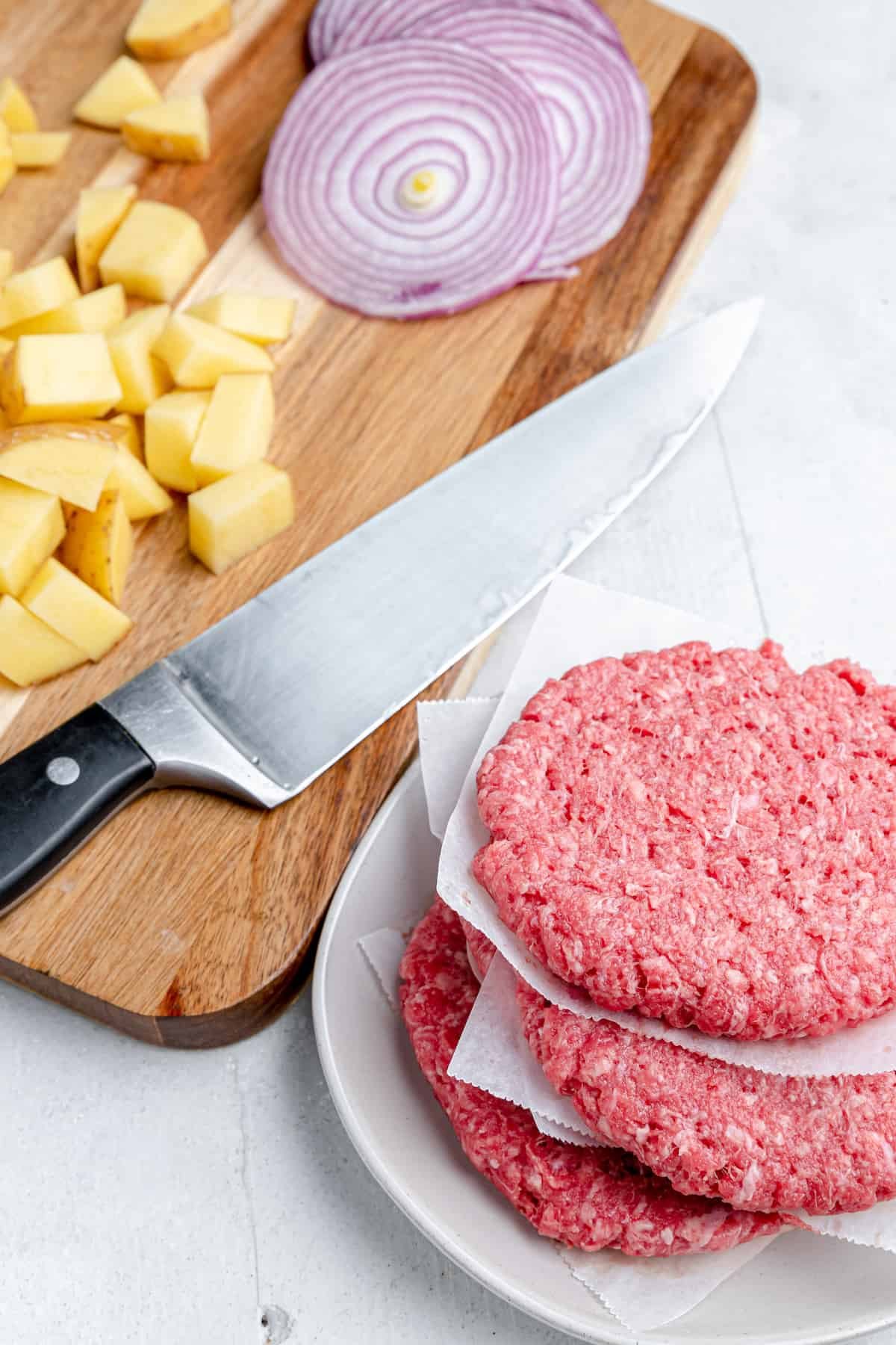 A beef patty, diced potatoes, onions and a knife
