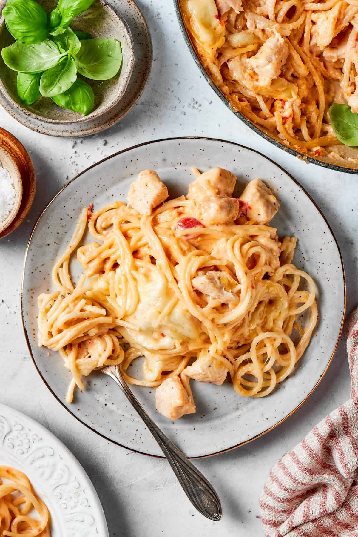 A plate of cheesy chicken spaghetti with a fork and a bowl of the spaghetti to the right.