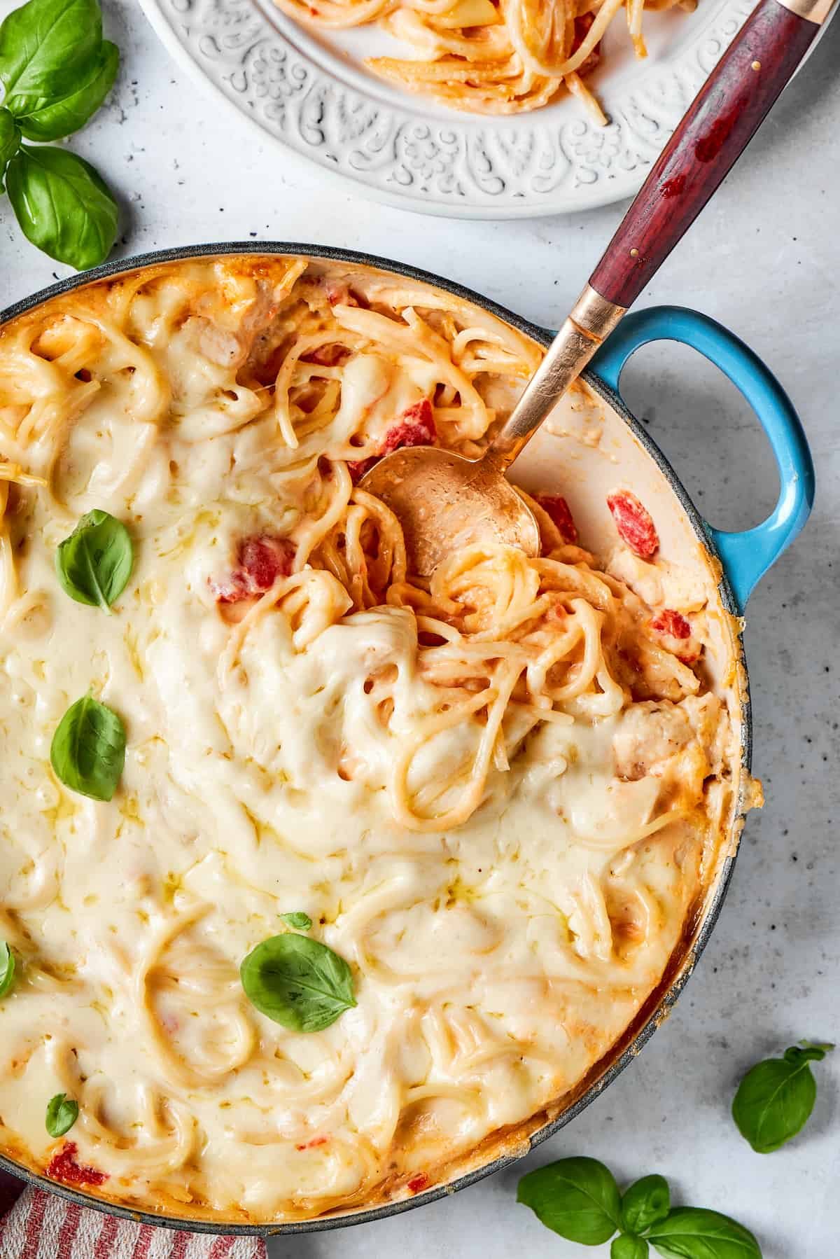 Basil is used as a garnish on a pot of cheesy chicken spaghetti with a serving spoon inserted into the pot.