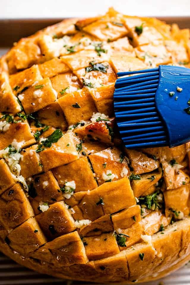 brushing loaf of bread with melted butter, garlic, and parsley