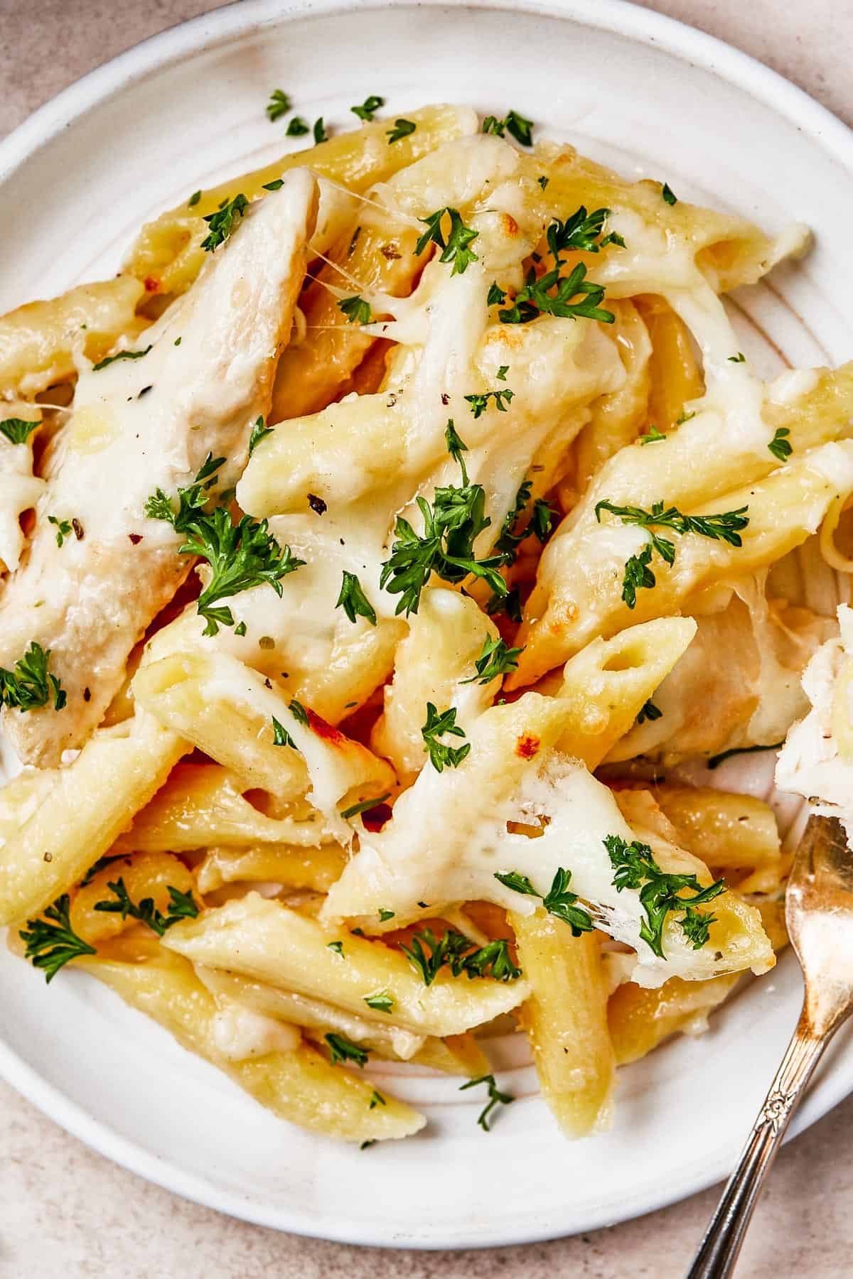 Overhead shot of chicken alfredo pasta bake on a plate, with a fork. The casserole dish is nearby on the table.