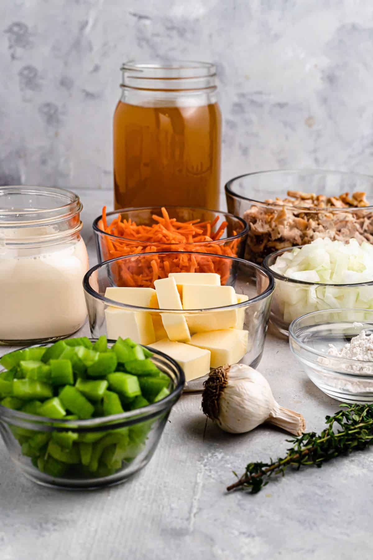 From the back row to the front row, left to right: Chicken broth, milk, matchstick carrots, cooked chicken, butter, diced onion, diced bell pepper, garlic, a sprig of thyme, flour.