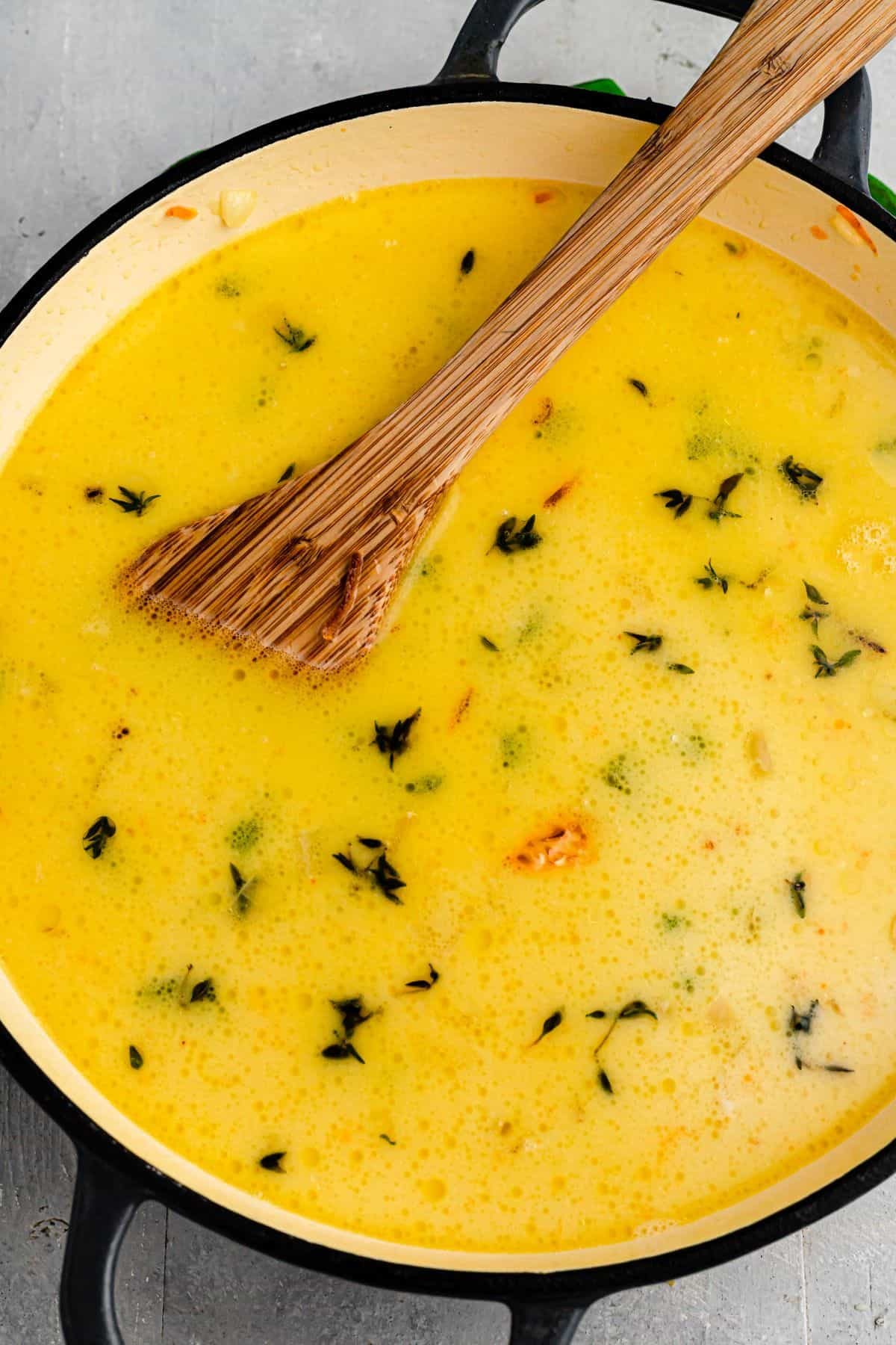 Creamy chicken broth in a Dutch oven with herbs floating on the surface.