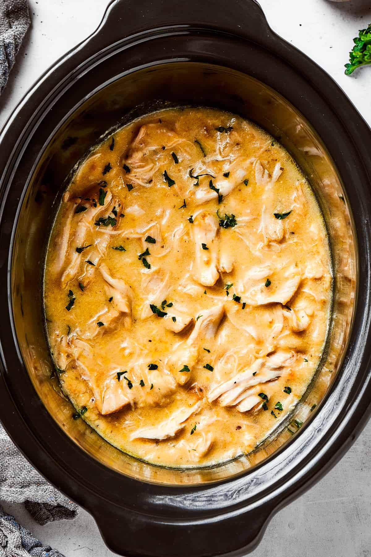 Overhead image of Shredded chicken in a creamy sauce cooking in a black slow cooker.