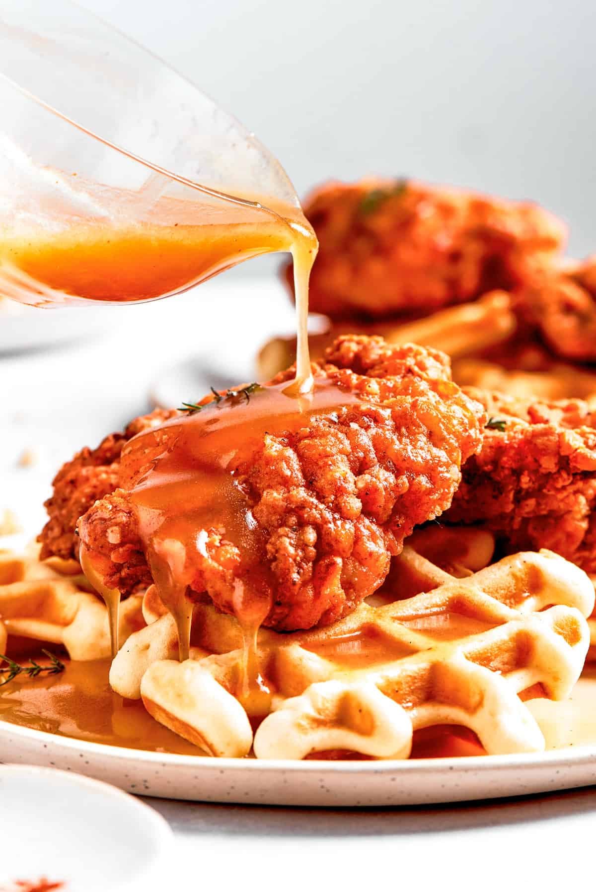 Pouring sauce over waffles and fried chicken.