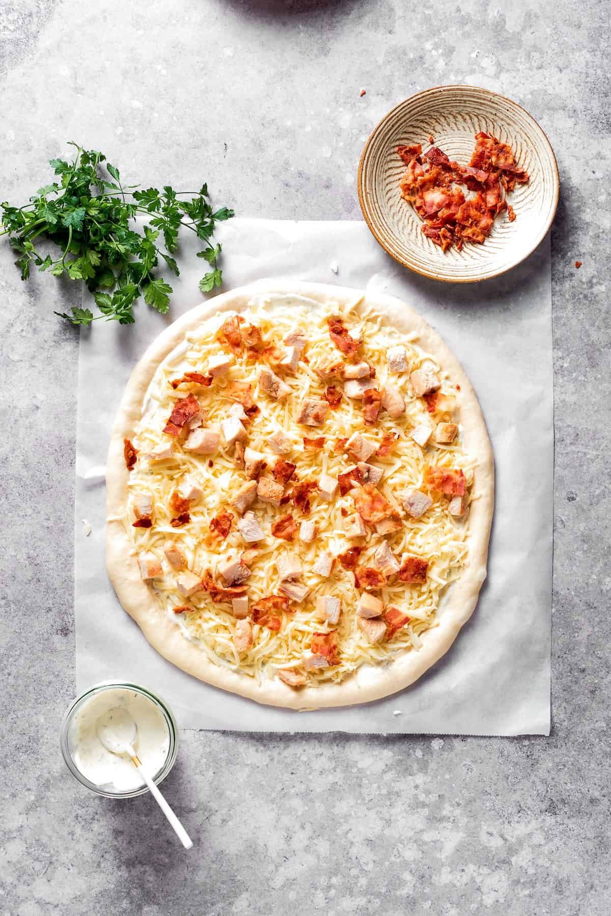 Bacon is added to the top of a chicken bacon ranch pizza.