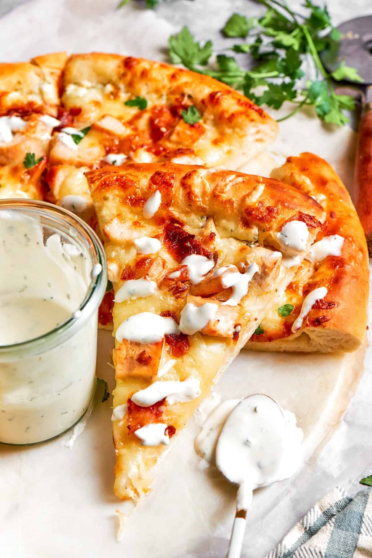Ranch sauce is drizzled on a slice of chicken bacon ranch pizza.