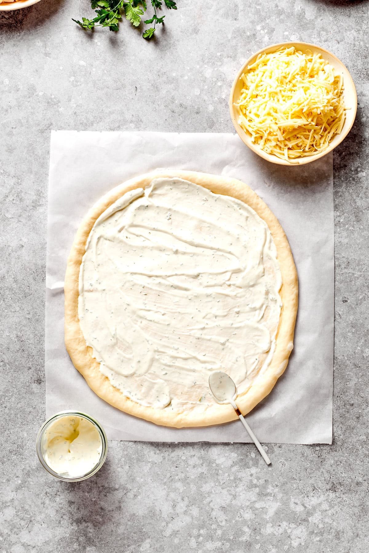A circle of pizza dough is topped with ranch dressing.