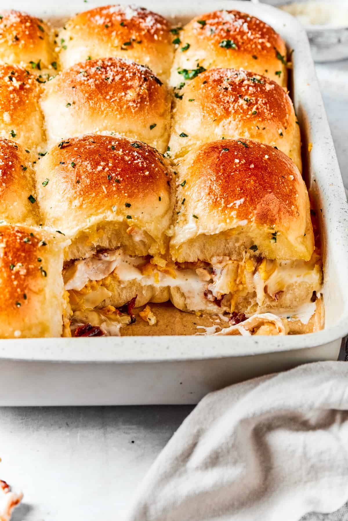 Chicken sliders in a baking dish with two of the sliders exposed so you can see the mixture inside.