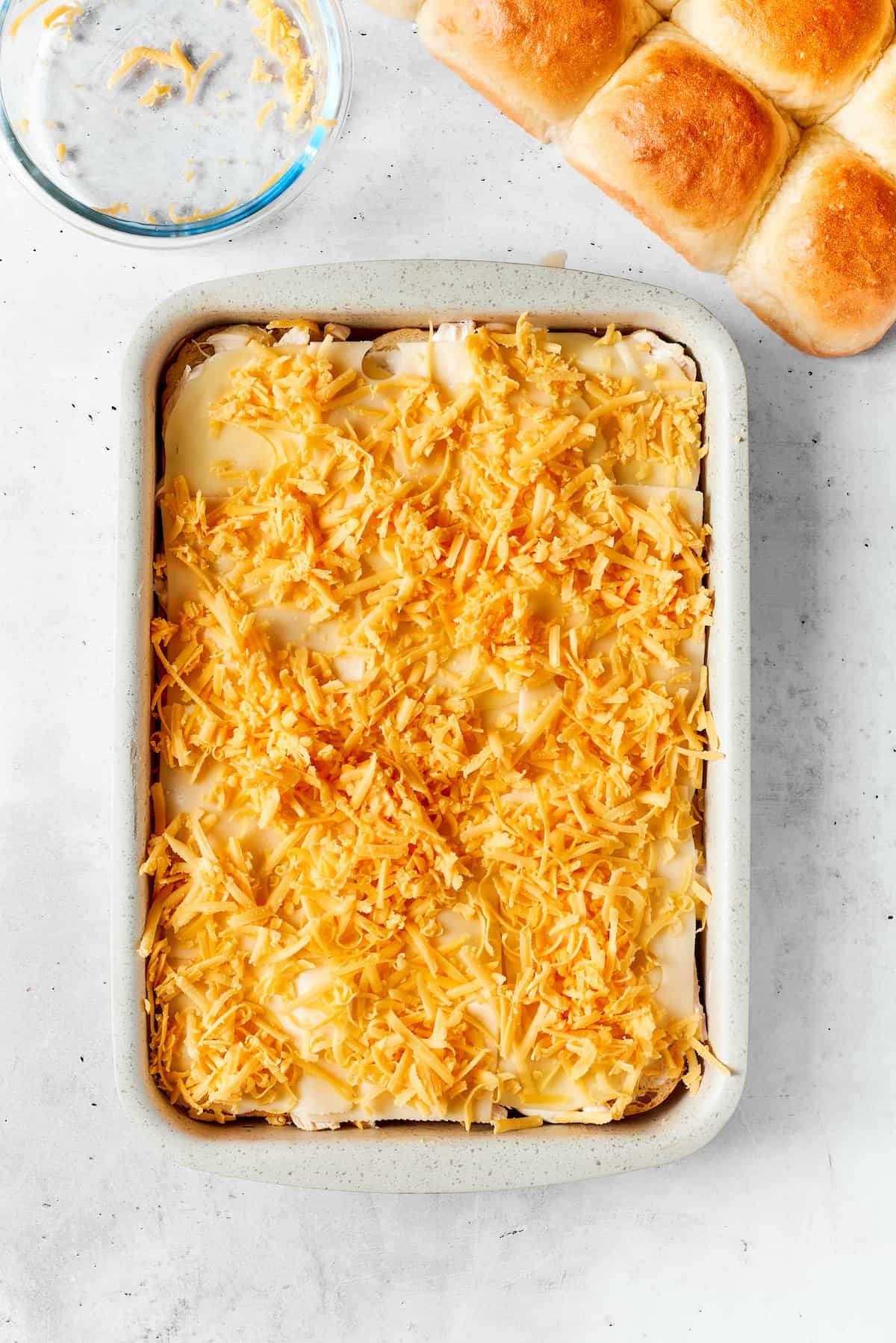 Shredded cheddar cheese is spread on the sliders.