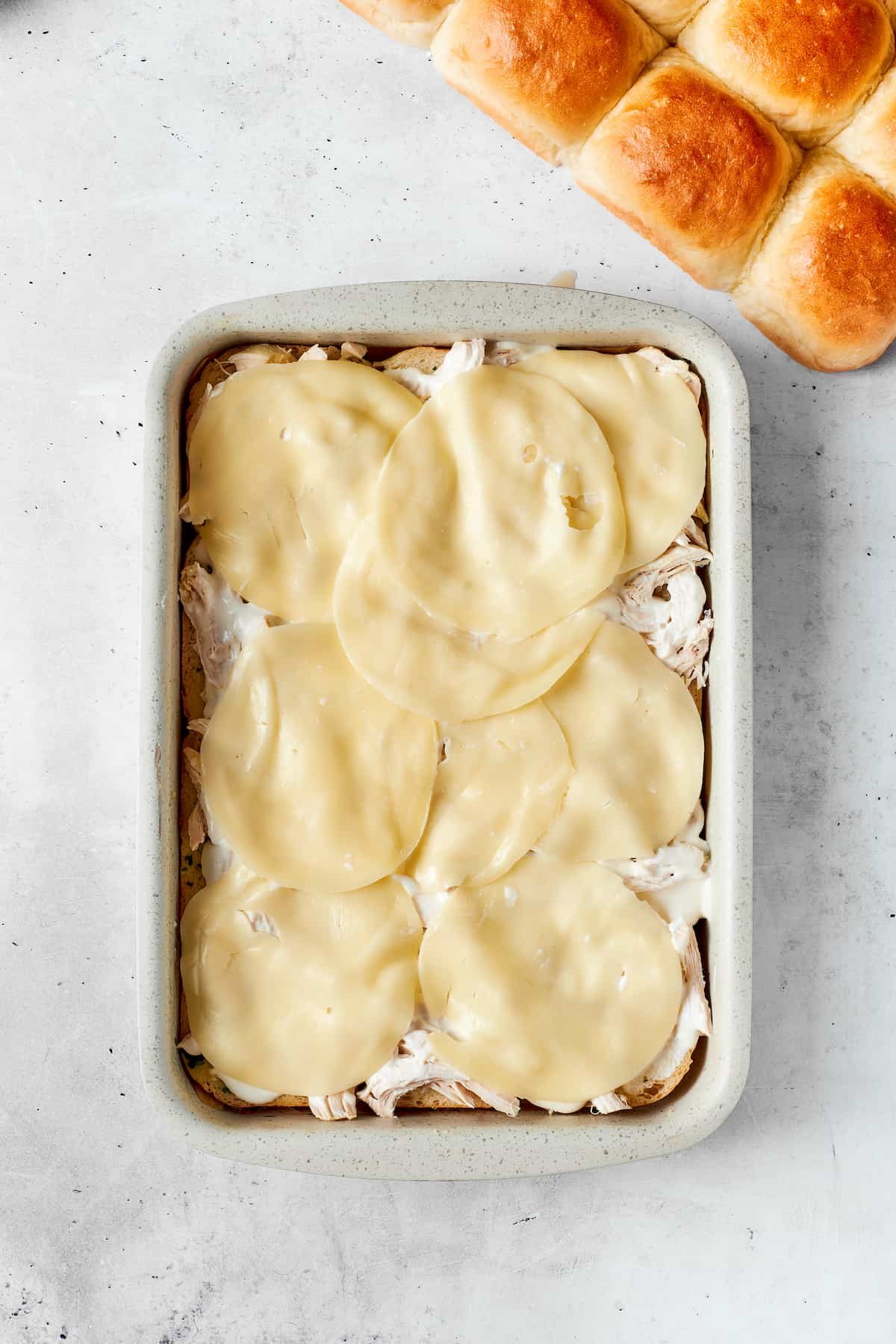 Slices of provolone cheese are placed on chicken bacon ranch sliders.