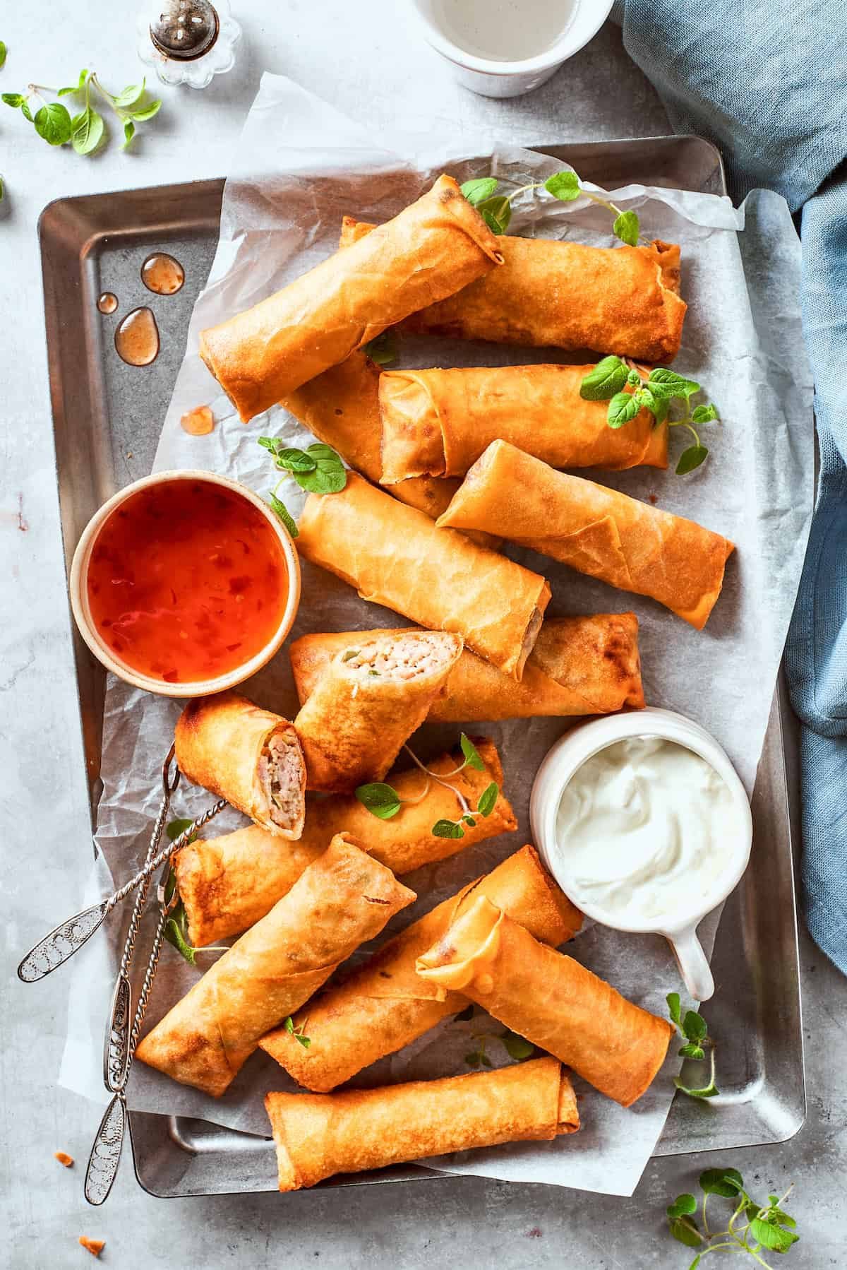A bowl of red sauce and a bowl of white sauce are served on a serving tray full of chicken egg rolls.
