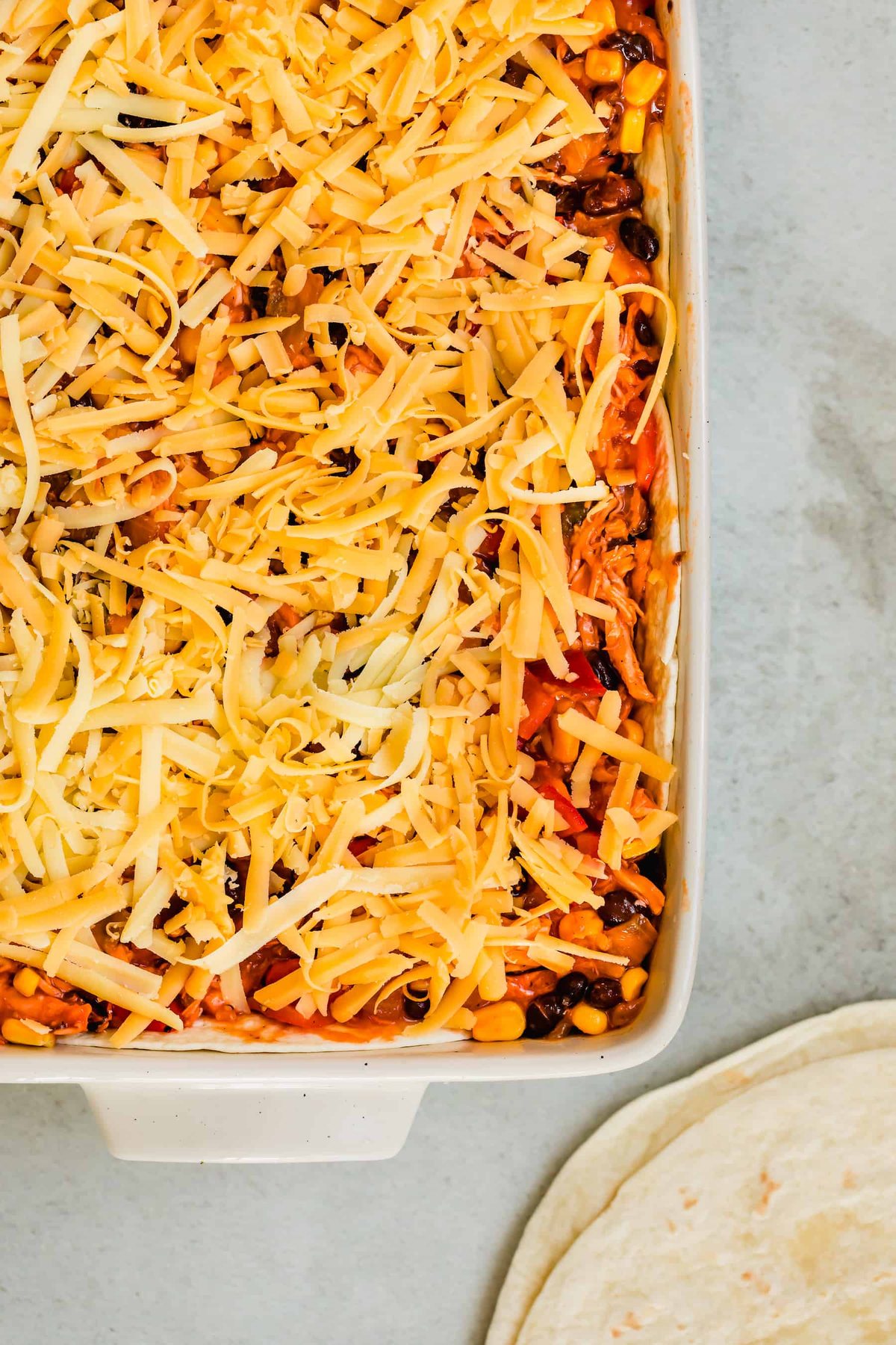 A Cheesy Chicken Enchilada Casserole in a Pan Beside Two Tortillas