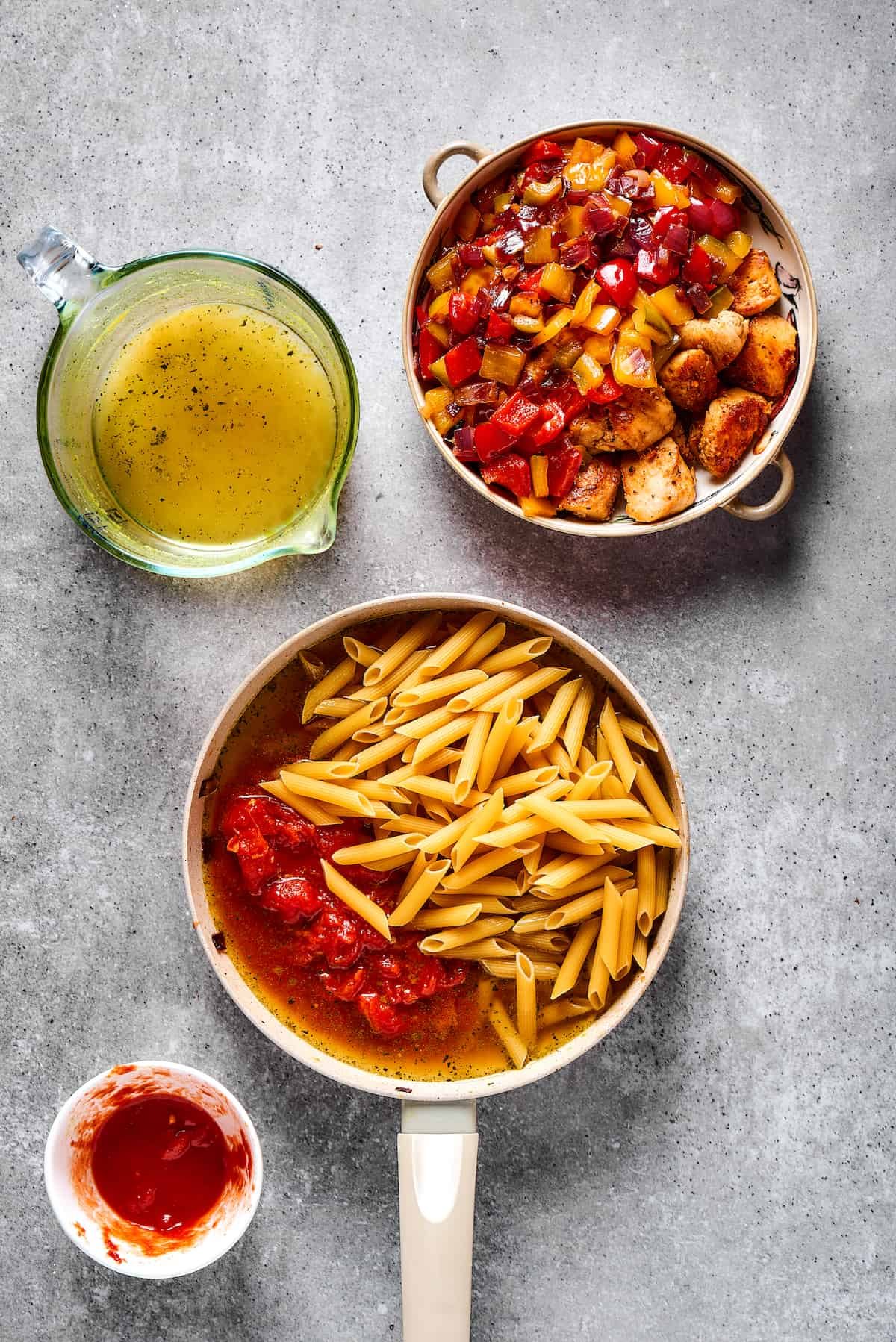 Pasta, tomatoes, and broth combined in a skillet next to a dish of cooked chicken and vegetables.