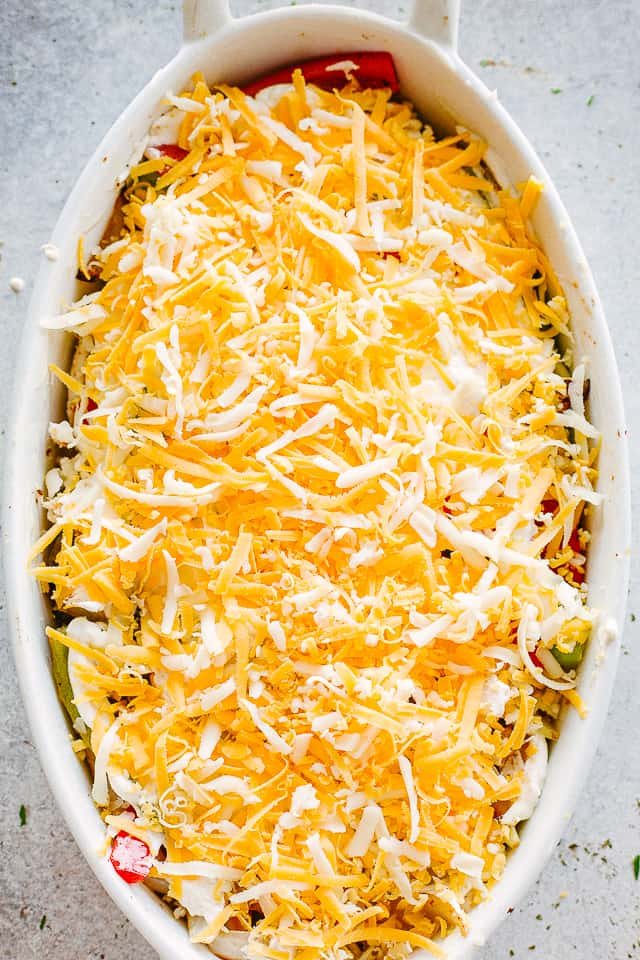 shredded cheese sprinkled over chicken and peppers in a white oval baking dish