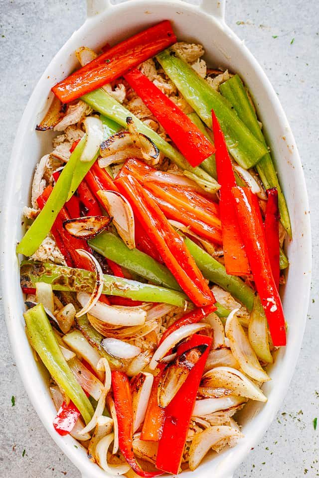 bell pepper strips arranged over shredded chicken in an oval baking dish