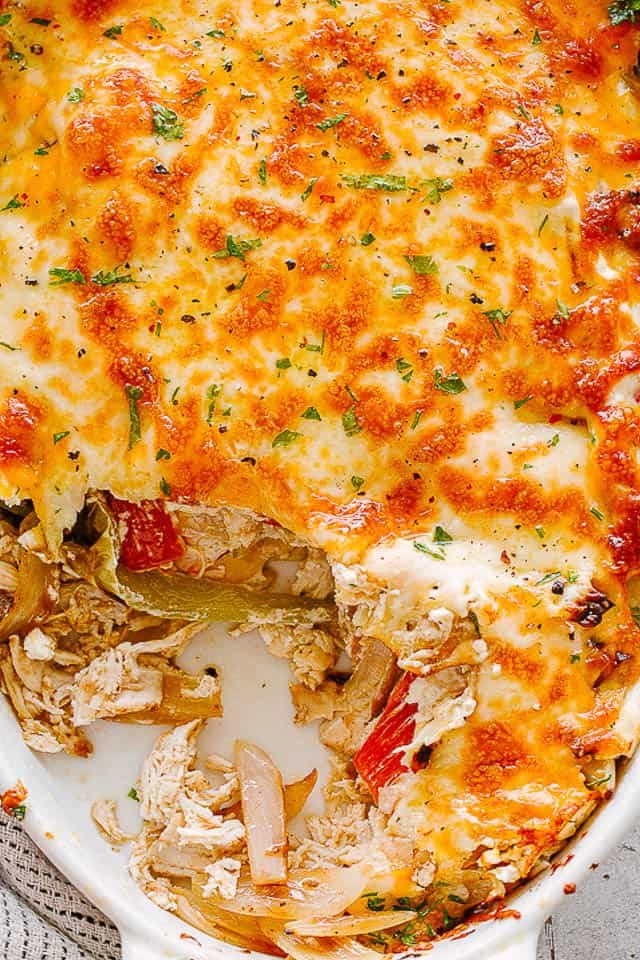 close up view of a chicken fajita casserole in a white oval baking dish
