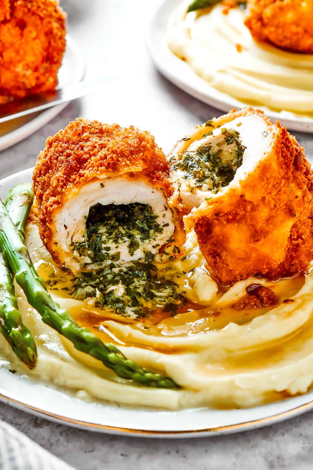 A serving of mashed. potatoes and asparagus with chicken Kiev cut in half to show the buttery filling.