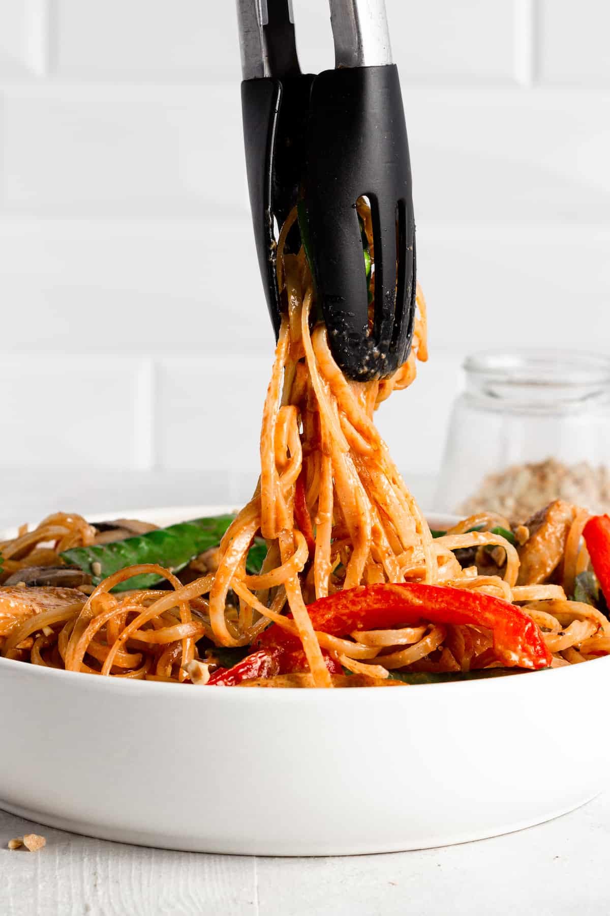 Tongs Scooping Up Some Noodles Out of a Bowl of Chicken Lo Mein