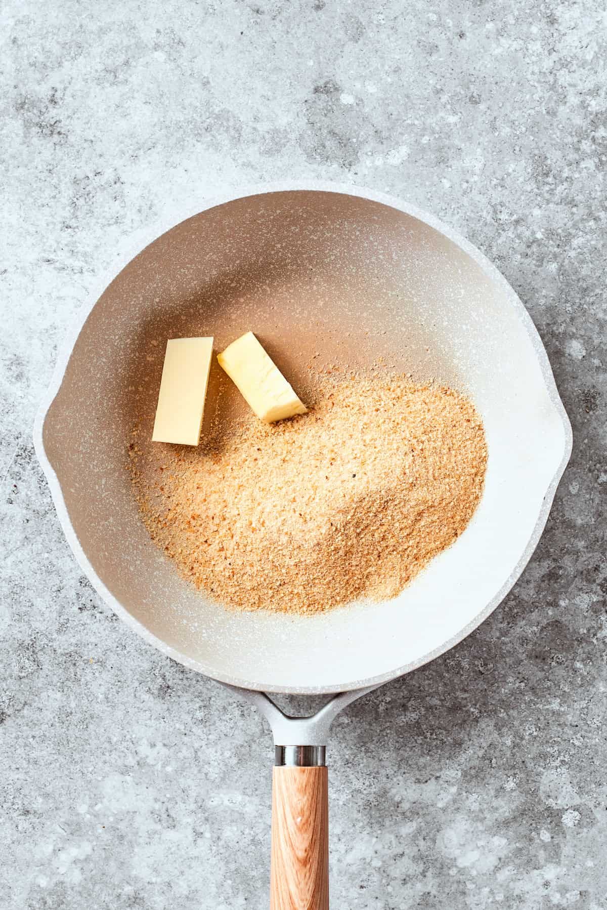 Butter is added to breadcrumbs in a pan.