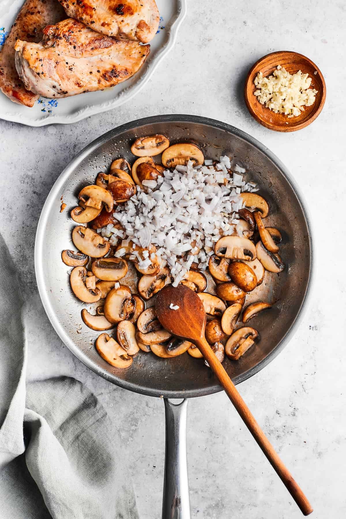 Garlic is added to a skillet of cooking mushrooms with a wooden spoon.
