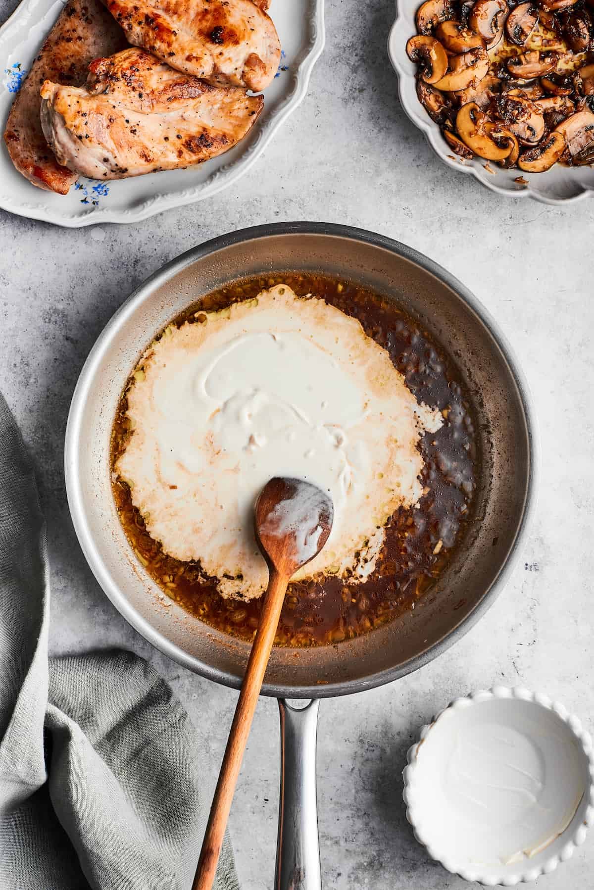 A wooden spoon stirs in heavy cream into the sauce for chicken madeira.