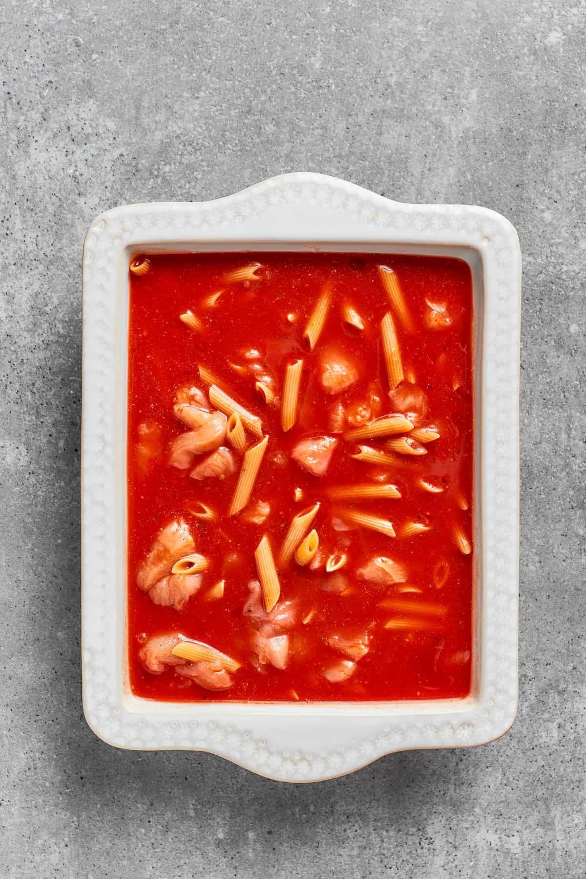Pasta is added to the sauce in the baking dish.