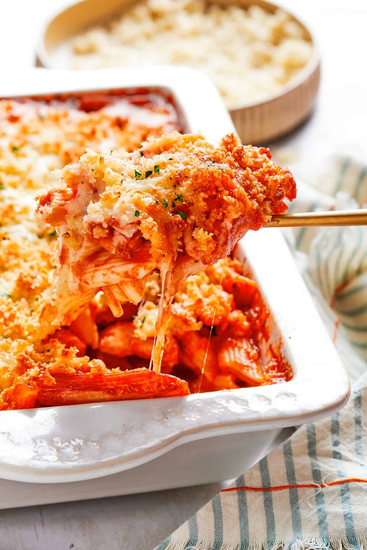 A spoon is pulling out chicken pasta from a baking dish.