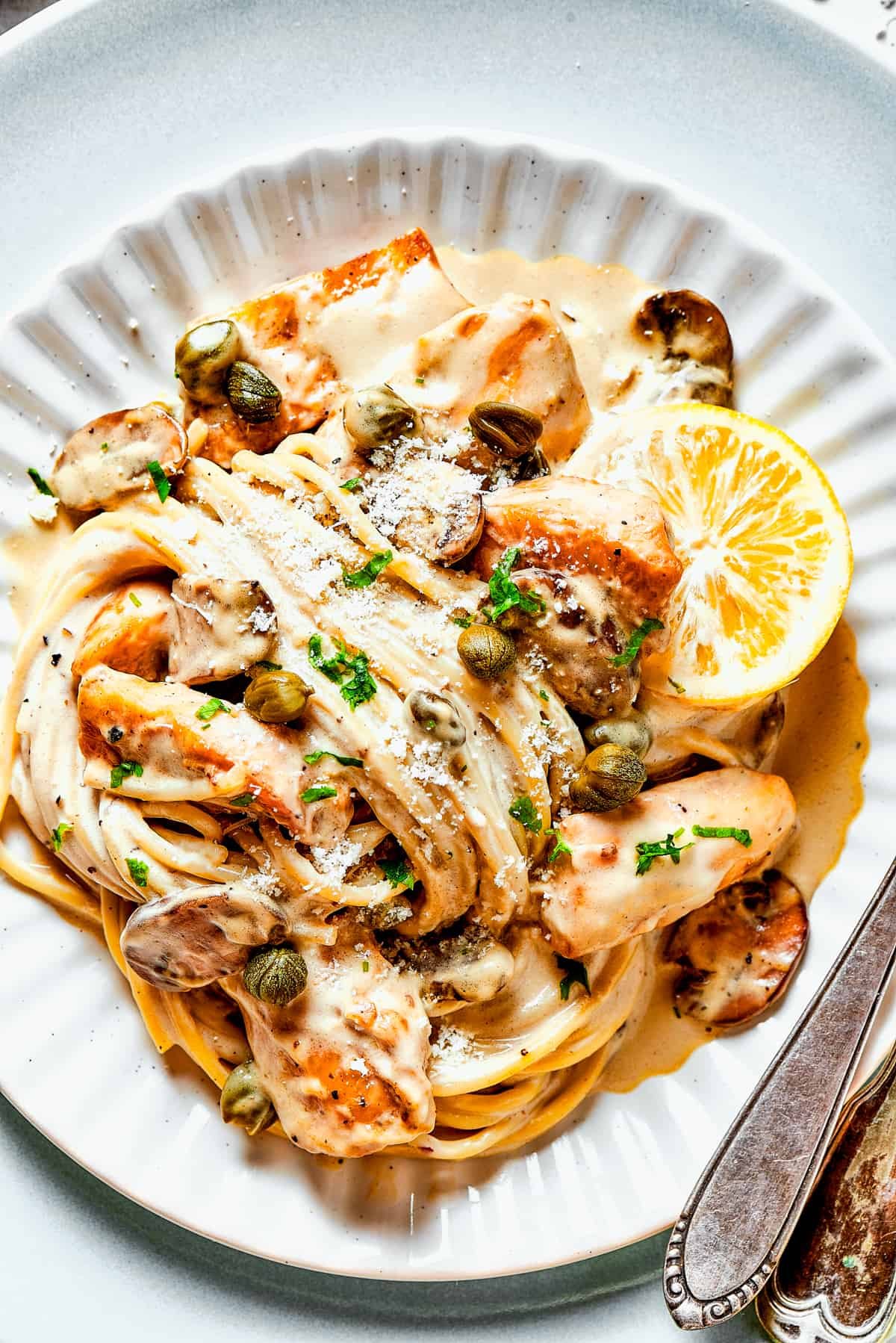 Chicken piccata in caper-lemon sauce with pasta and served on a dinner plate.