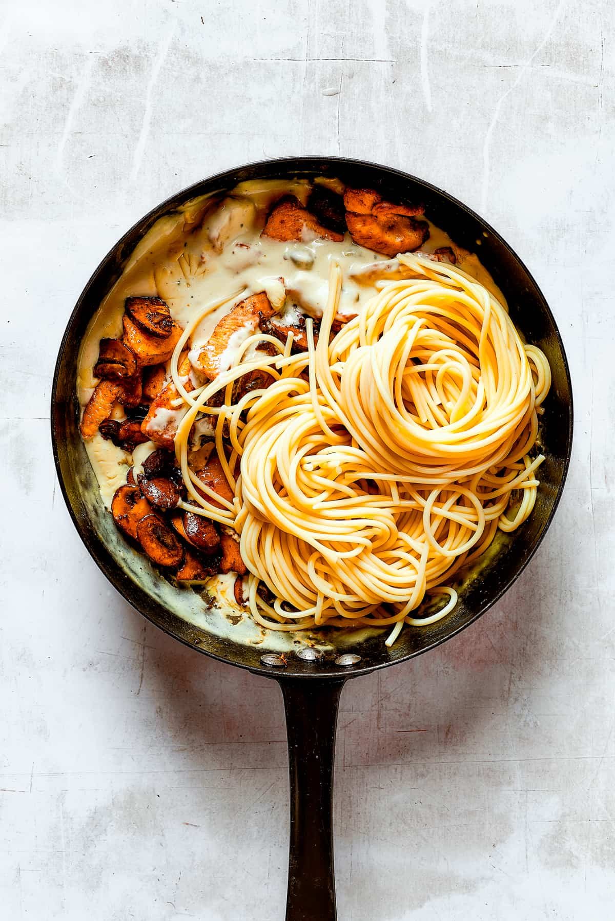 Adding mushrooms, chicken, and pasta to a skillet.