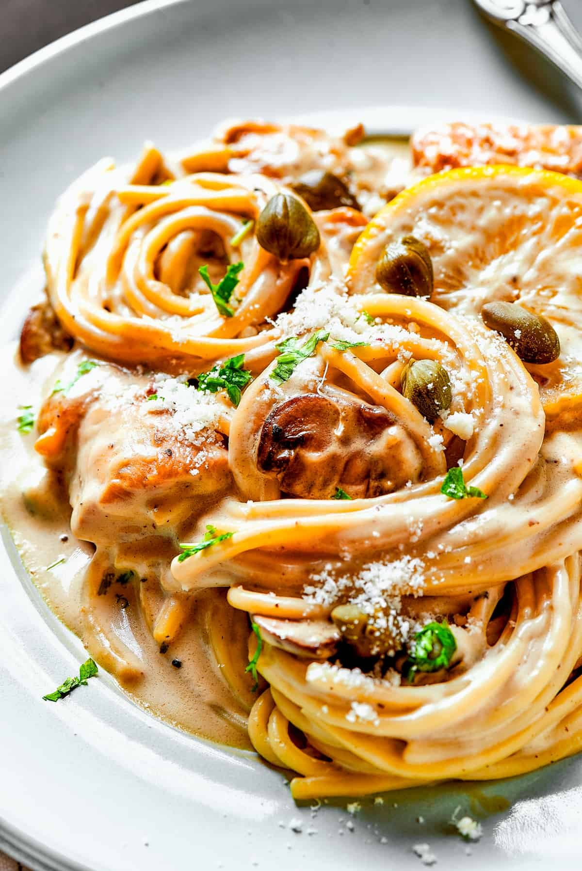 Close-up shot of creamy pasta with capers, lemon, and chicken.