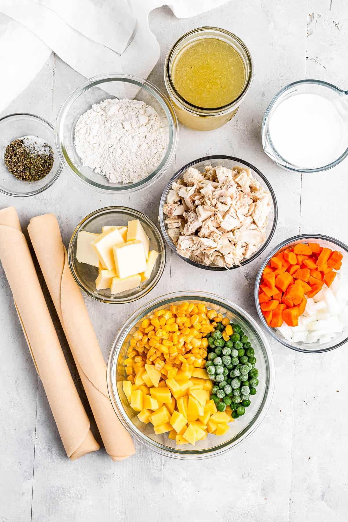 Clockwise from top: chicken broth, milk, chopped carrots and onions, a bowl of peas, corn, and diced potatoes, butter, seasonings, and flour.