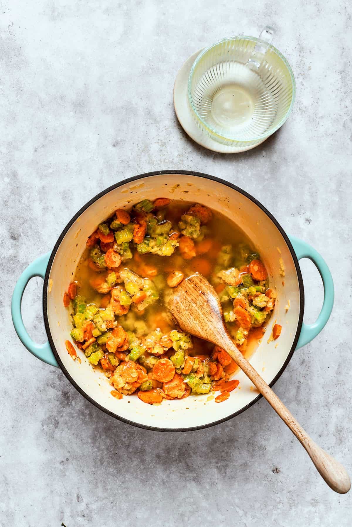 Adding broth to veggies in a large pot.