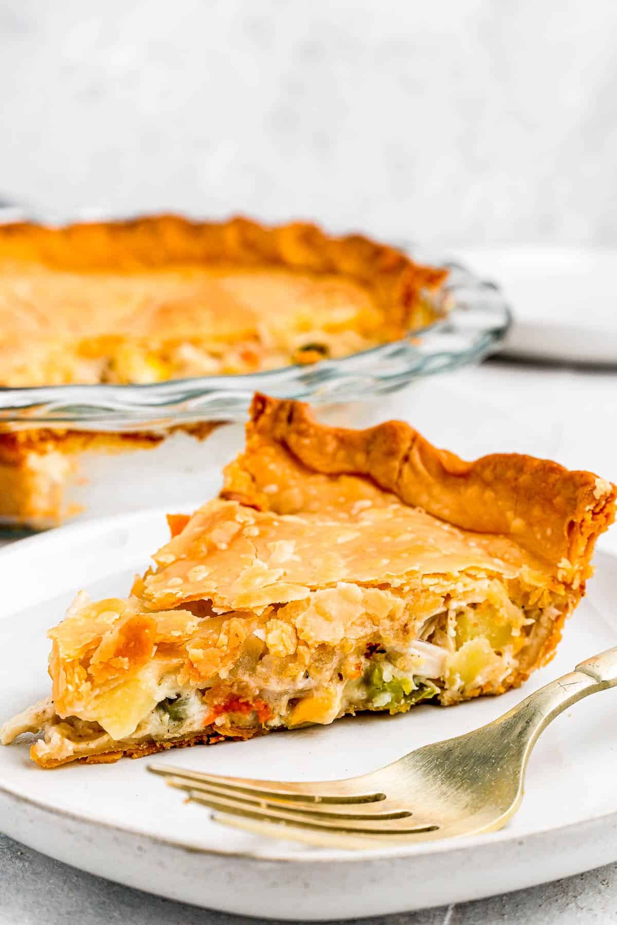 In the background, the baked chicken pot pie. In the foreground, a slice of the pie on a plate with a fork.