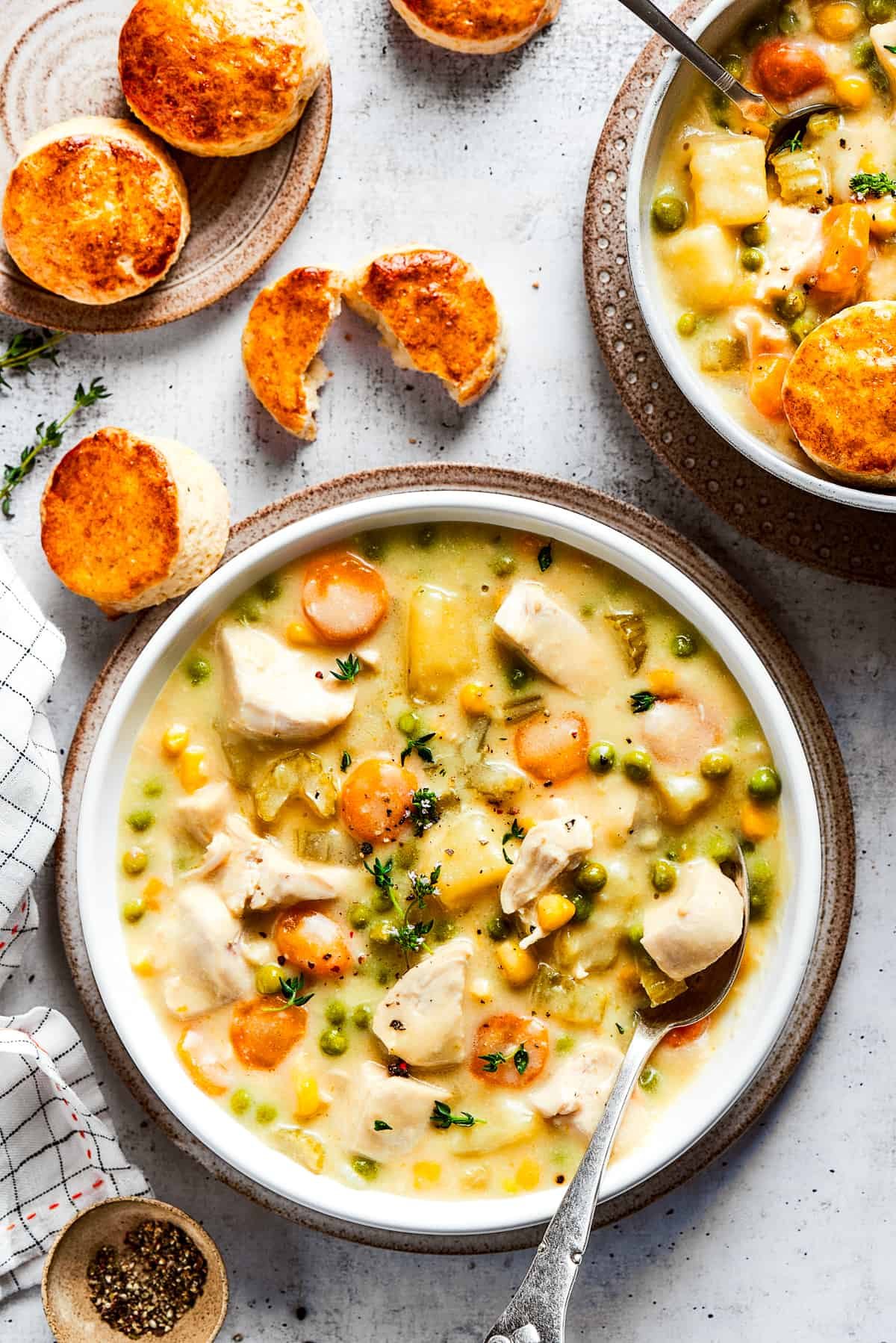 A bowl of chicken pot pie soup topped with a spoon in it, and a plate of biscuits in the background.