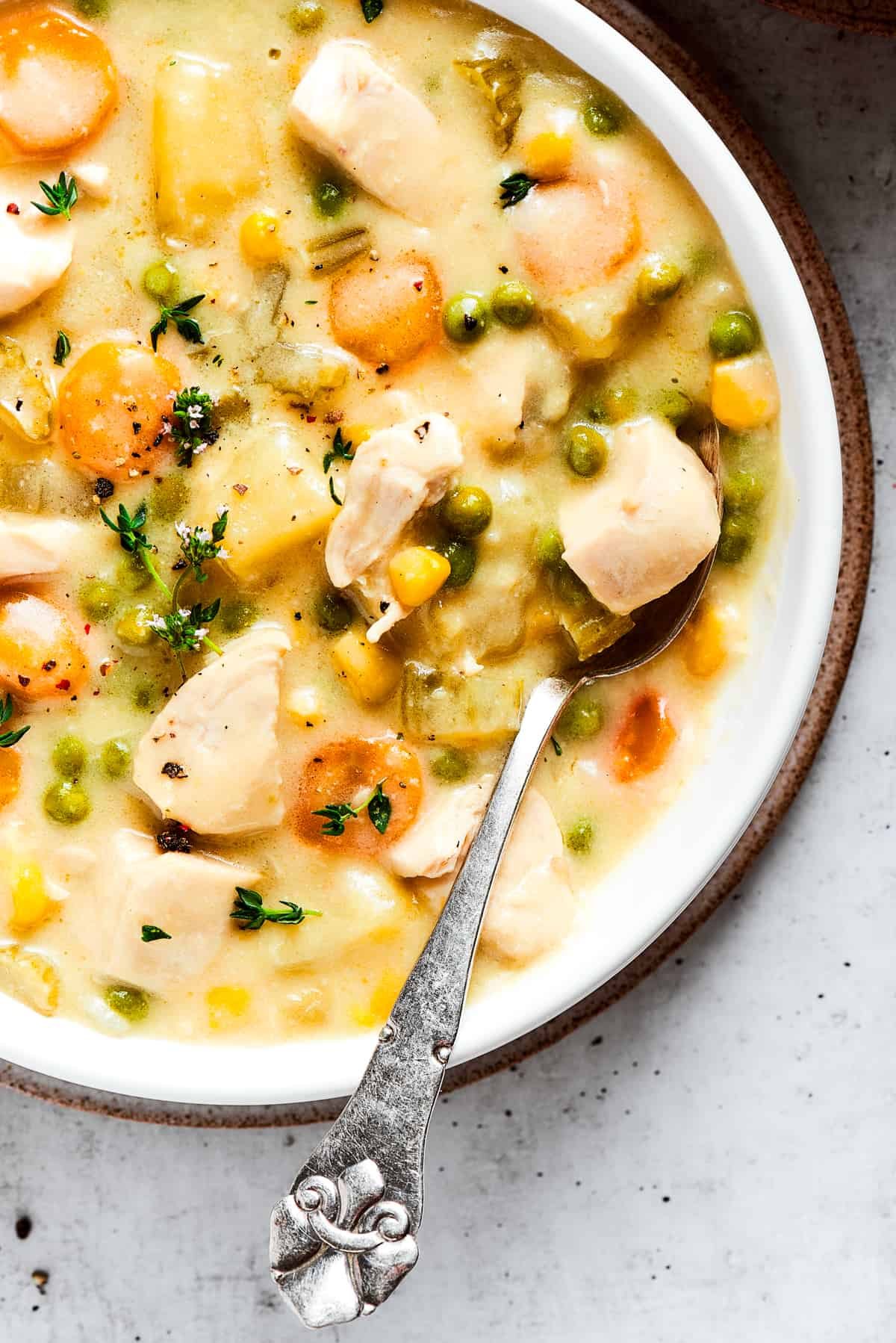 Close-up image of a bowl with chicken pot pie soup, topped with thyme, with a spoon resting in the bowl.