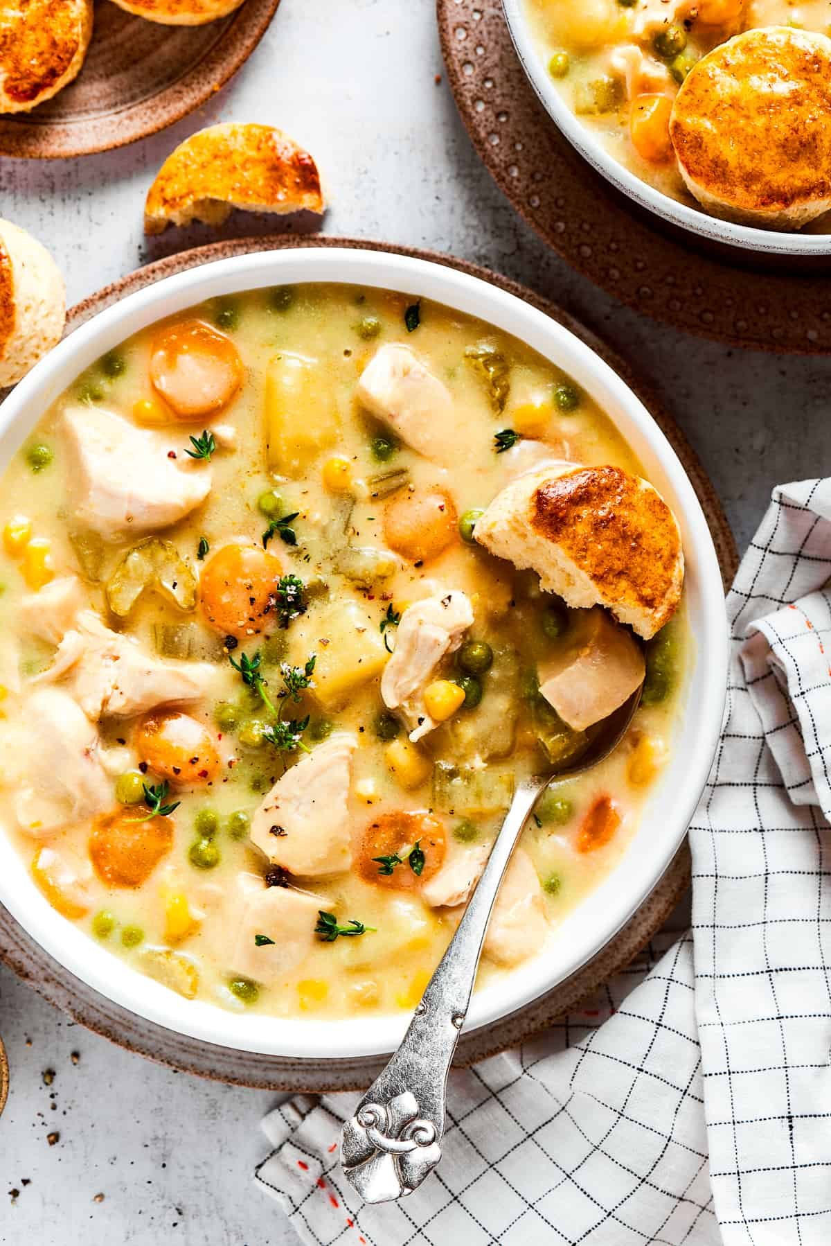 Overhead view of a bowl of chicken pot pie soup garnished with thyme, next to some biscuits.