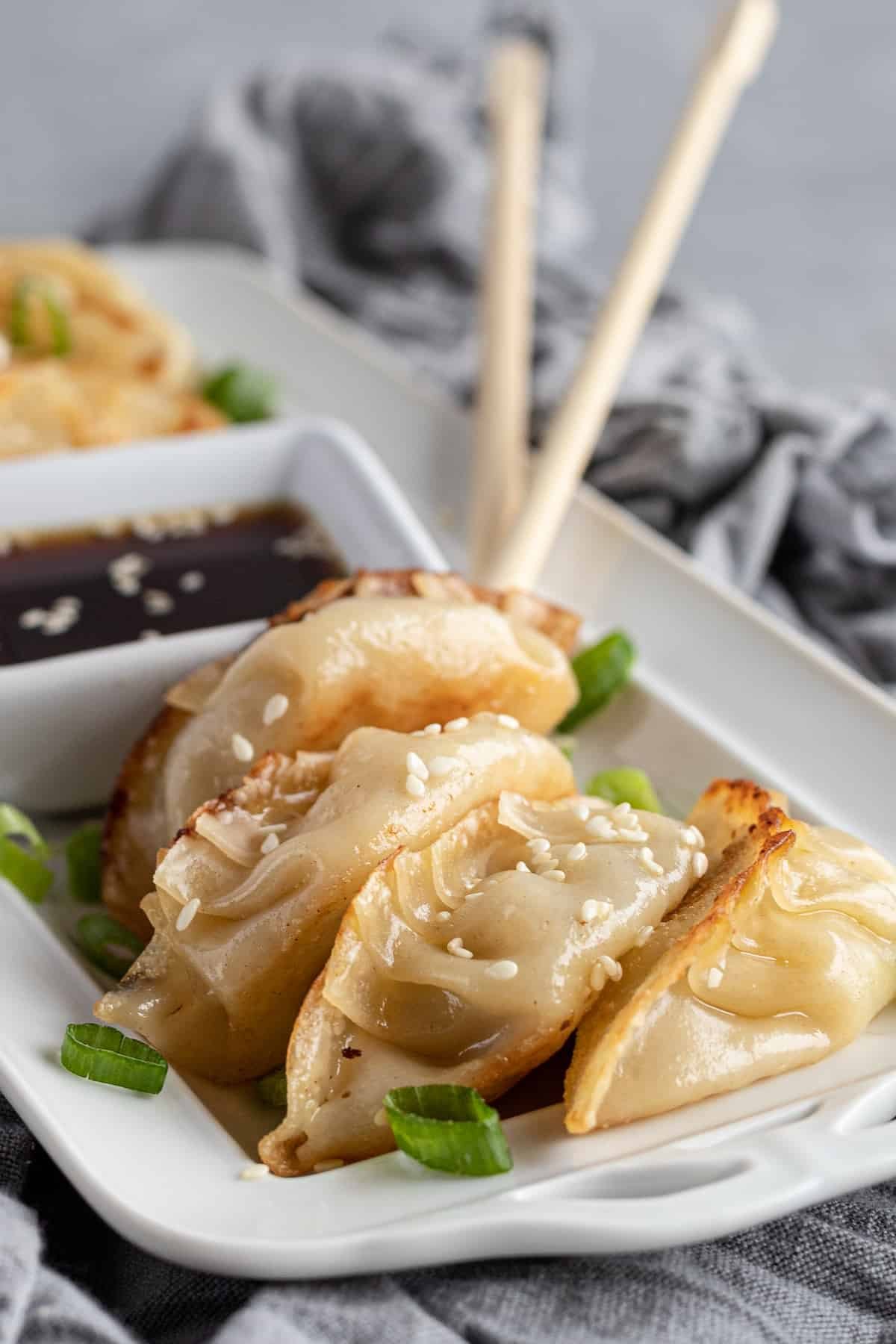 Four Chicken Potstickers on a Serving Platter with Two Chopsticks in the Background