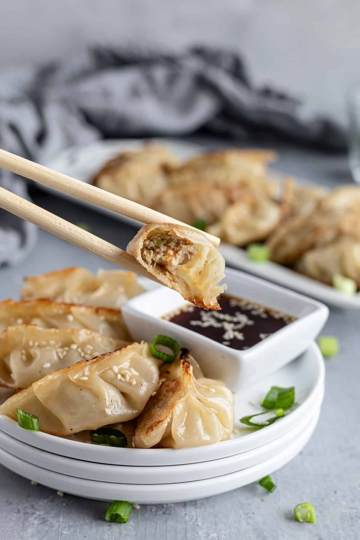 A Chicken Potsticker Being Held by a Pair of Wooden Chopsticks