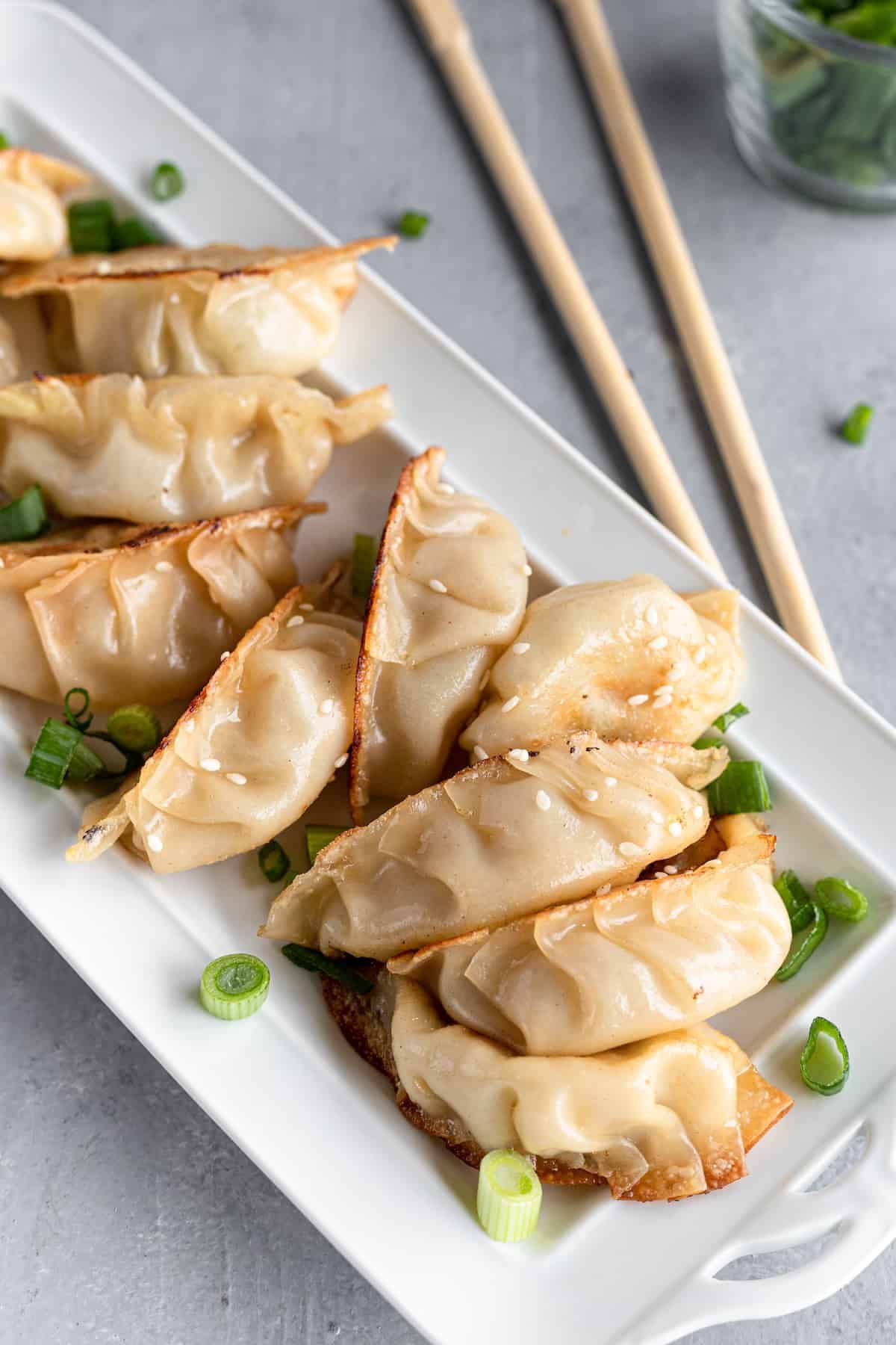 Ten Chicken Potstickers on a White Serving Platter Beside a Pair of Chopsticks