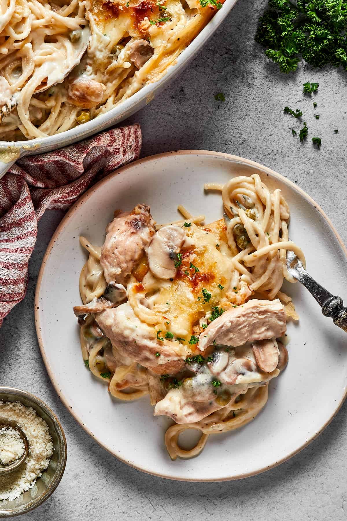 A dinner plate of pasta casserole next to the larger casserole dish, on a white table.
