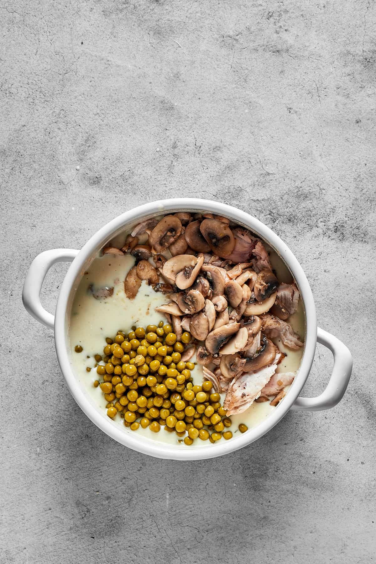 Musrooms, cream, peas, and other ingredients added to a pot.