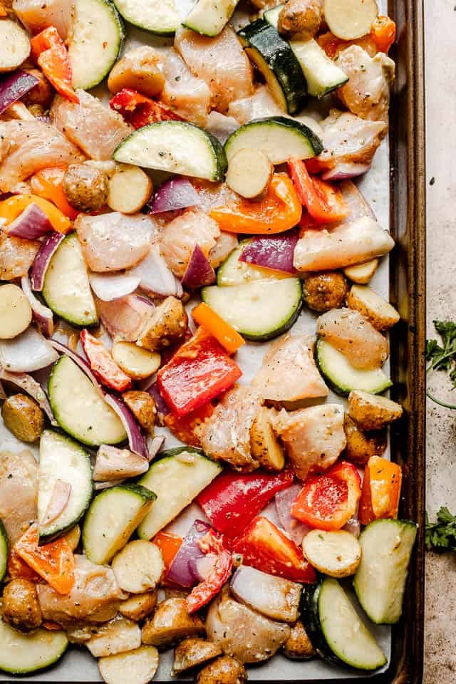 prepping raw chicken and vegetables on a baking sheet
